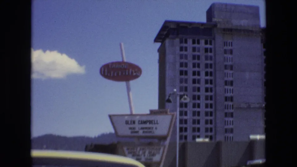 1973 Lake Tahoe, Nevada frame with the Tahoe Harrah's oval sign above a marquee advertising Glen Campbell, backed by a tall hotel tower and blue sky.