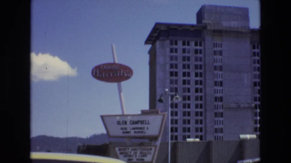 1973 Lake Tahoe, Nevada frame centering the Tahoe Harrah's sign and Glen Campbell marquee, with the hotel tower, hills, sky, and roadside foreground visible.