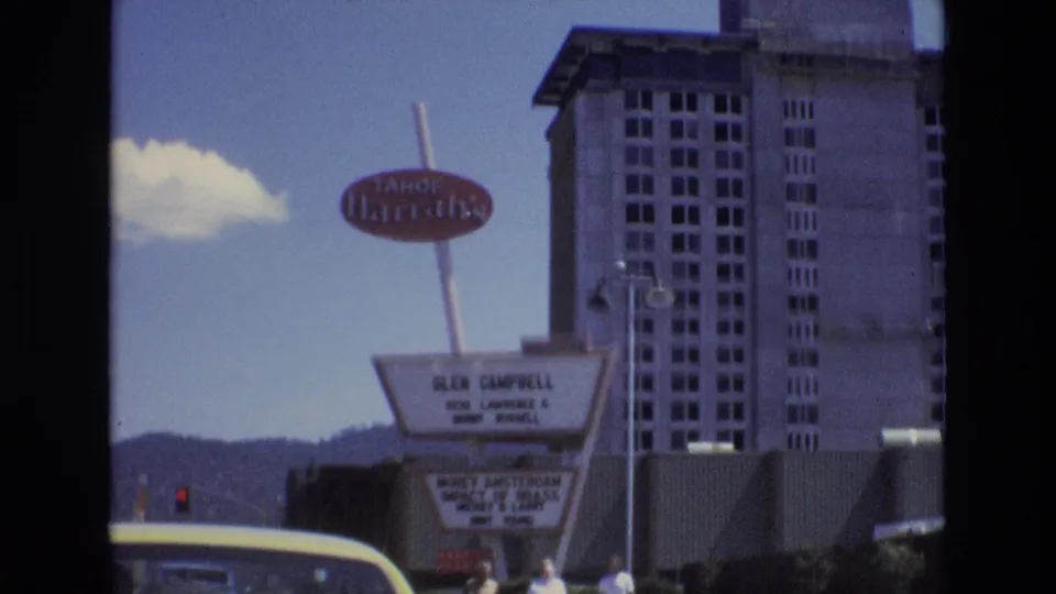 1973 Lake Tahoe, Nevada frame showing Tahoe Harrah's signage, the hotel tower, marquee lettering, a yellow car roof, and small distant people near the lower right edge.