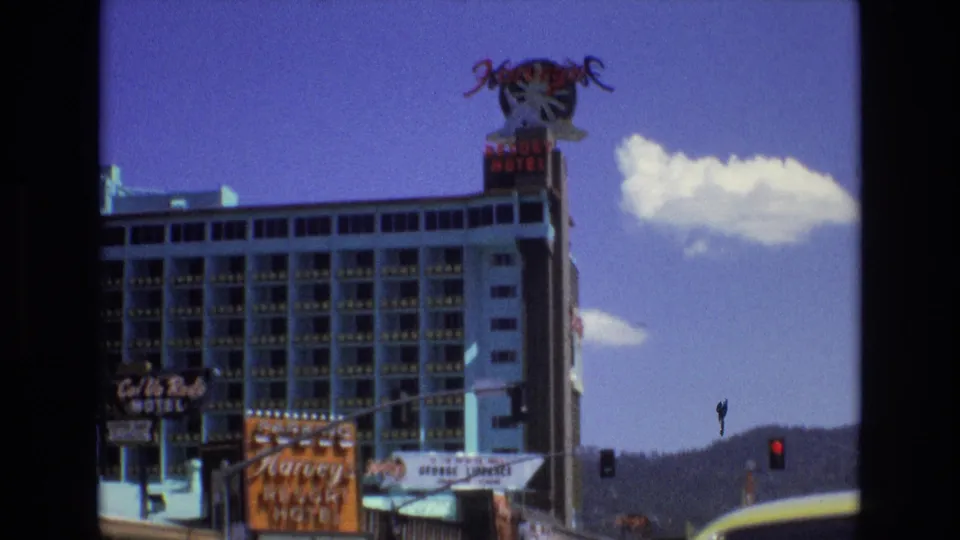1973 Lake Tahoe, Nevada street frame showing Harvey's Resort Hotel signage, a tall hotel facade, motel and billboard signs, traffic lights, mountain backdrop, and the edge of a vehicle in the foreground.