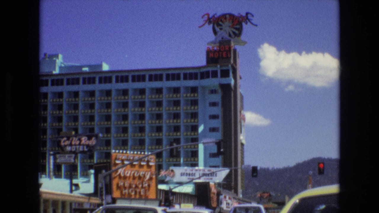 Harvey's Resort Hotel exterior with neon signage, traffic lights, cars, mountains, and blue sky.