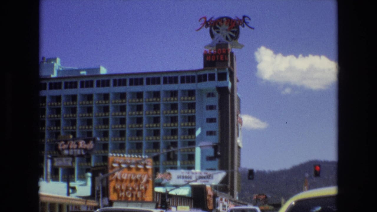 Resort hotel facade with Harvey's signage, nearby motel signs, traffic signal, cars, and mountains.