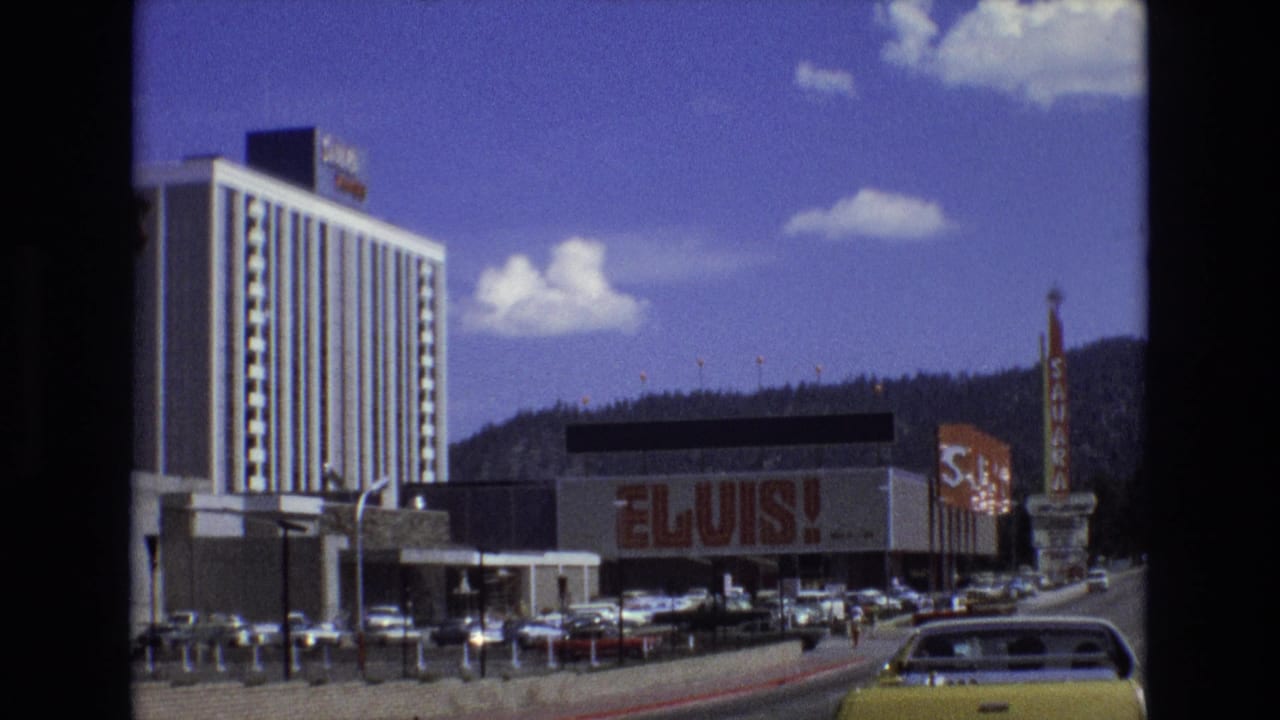 Street scene with Elvis sign on a building, tall hotel, cars, and Sahara sign.