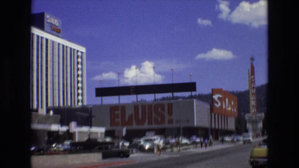 1973 Lake Tahoe, Nevada 8mm frame showing the Sahara hotel exterior with a large ELVIS! facade sign, period cars, pedestrians, and mountains in the background.