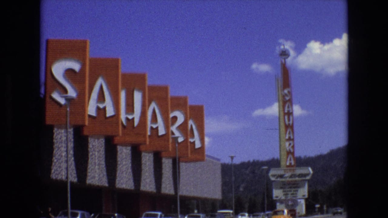 1973 Lake Tahoe, Nevada view of large orange Sahara sign panels beside the hotel, with the vertical Sahara tower sign, parked cars, mountains, and clouds visible.
