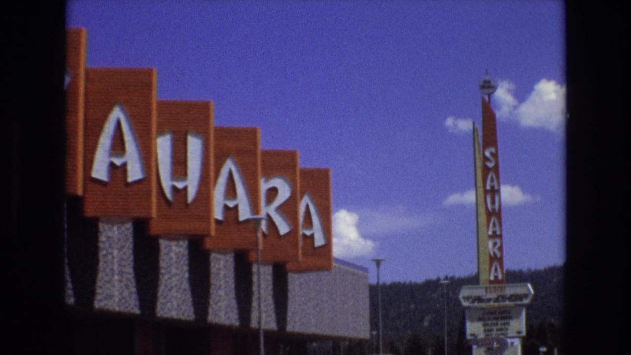 1973 Lake Tahoe, Nevada home-movie frame showing large red Sahara hotel lettering at left, a vertical Sahara sign, blue sky, clouds, and mountain backdrop.