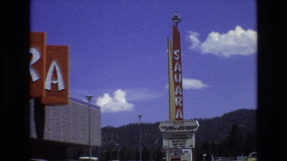 1973 Lake Tahoe, Nevada frame with the camera panning past partial Sahara letters toward the tall vertical sign and marquee below against clouds and mountains.