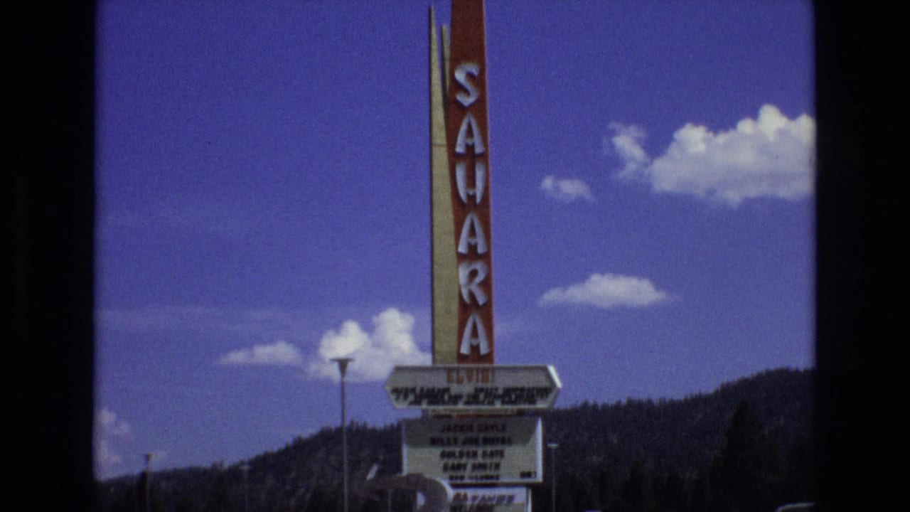 1973 Lake Tahoe, Nevada frame showing the tall Sahara sign above a marquee that appears to advertise Elvis, with clouds and a wooded mountain ridge in the background.