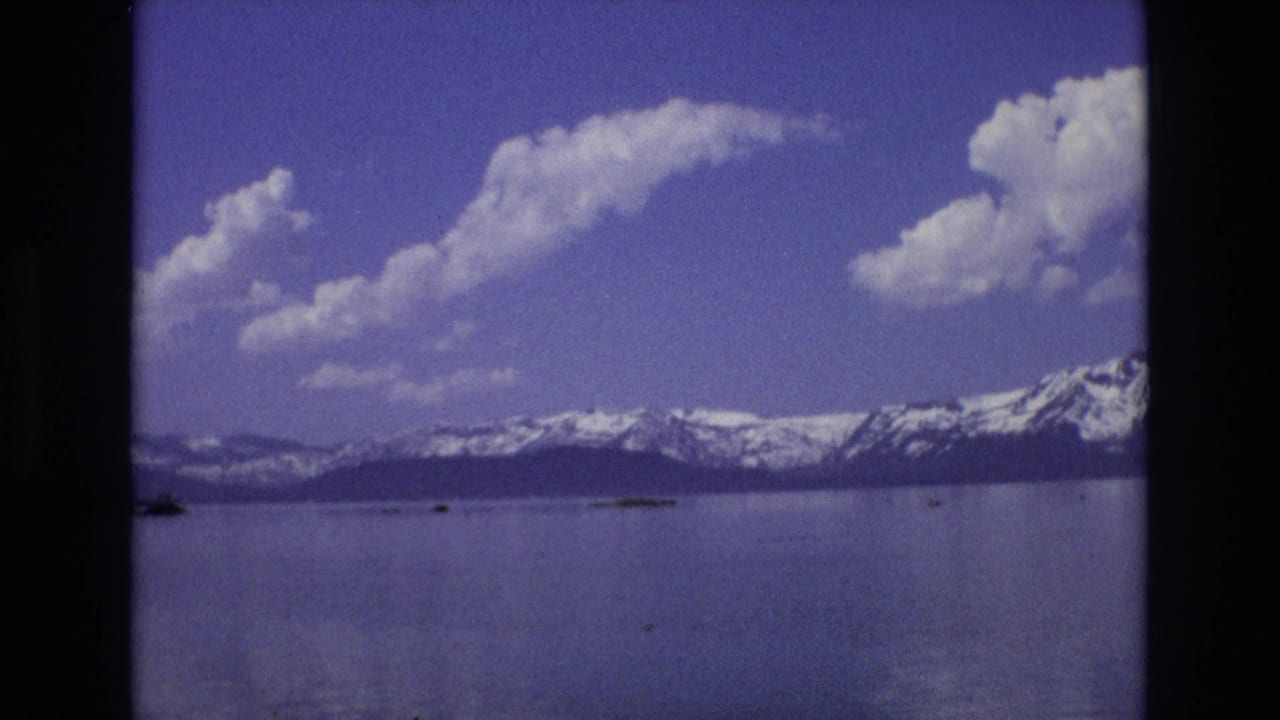 Snowy mountain range across a still lake under a blue sky with white clouds.