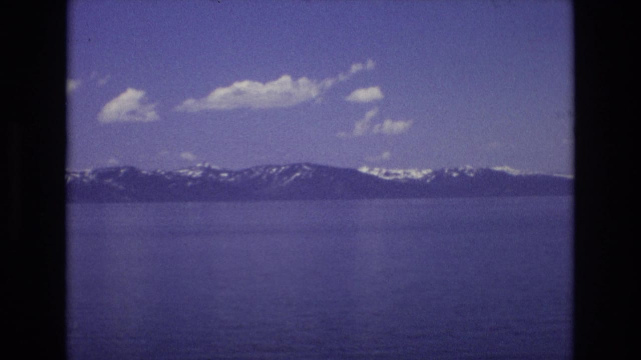 Distant mountain range across a broad lake under a bright clouded sky.