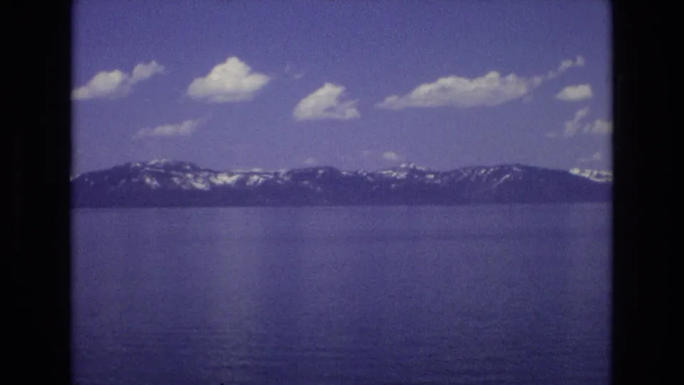 Final 8mm frame from the Lake Tahoe view, showing broad water, distant snow-marked mountains, scattered clouds, and the soft color shift of the scanned home movie.