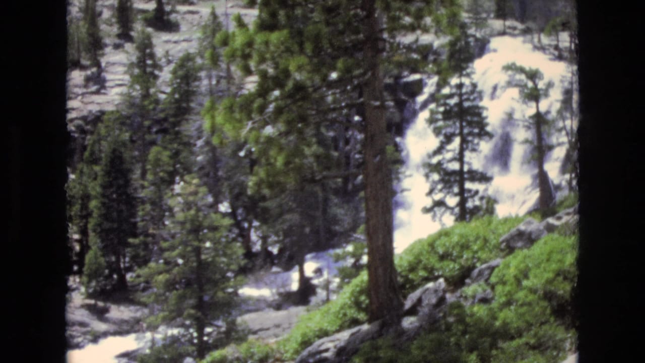1973 Lake Tahoe, Nevada 8mm frame showing white water dropping through rocks with pine trunks and green forest growth in the foreground.
