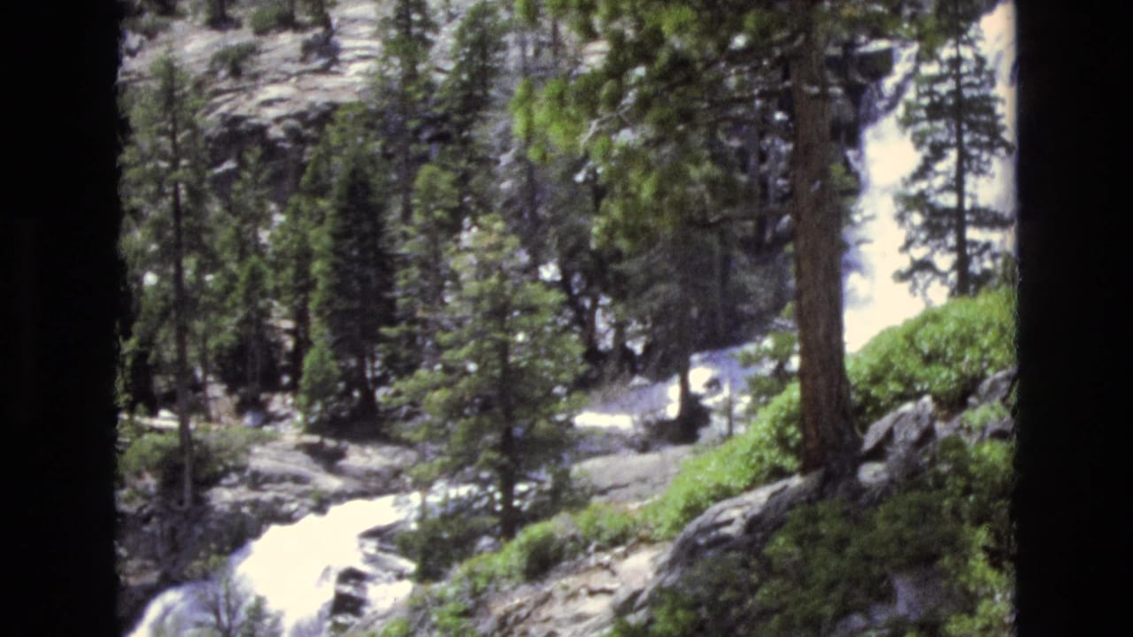 1973 Lake Tahoe, Nevada 8mm frame with a bright white stream running below tall pines, rocky terrain, and dense evergreen growth.