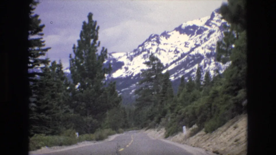 1973 Lake Tahoe, Nevada home-movie view from a moving car on a mountain road lined with evergreens and roadside posts.