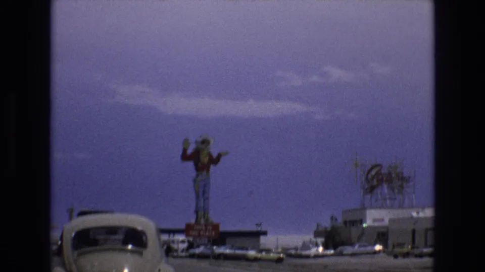 1973 Lake Tahoe, Nevada frame with the cowboy figure centered above a low commercial roadside area, a Volkswagen Beetle at left, and signage visible on a building roof.