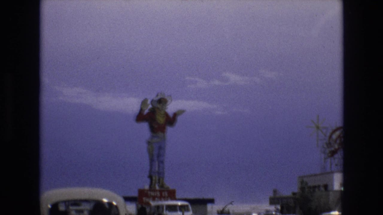 Large cowboy statue beside a road with cars under a purple-blue sky.