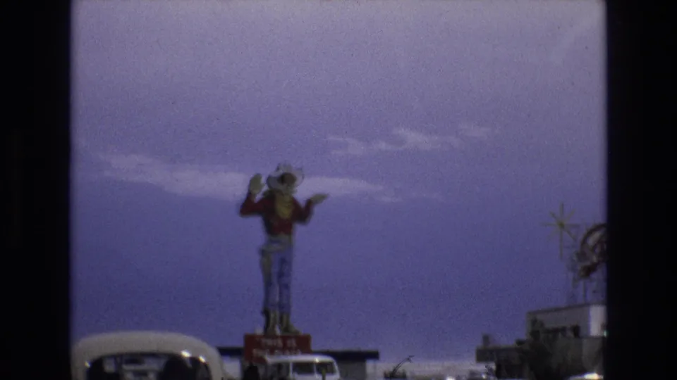 1973 Lake Tahoe, Nevada roadside view with a large waving cowboy statue above a red sign and classic cars passing in the foreground.