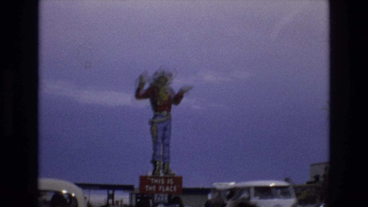 Cowboy statue on a sign with cars and roadside structures below.
