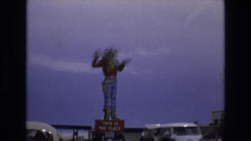 A large novelty cowboy figure stands above a readable attraction sign as vehicles pass through a Lake Tahoe roadside area in 1973 footage.