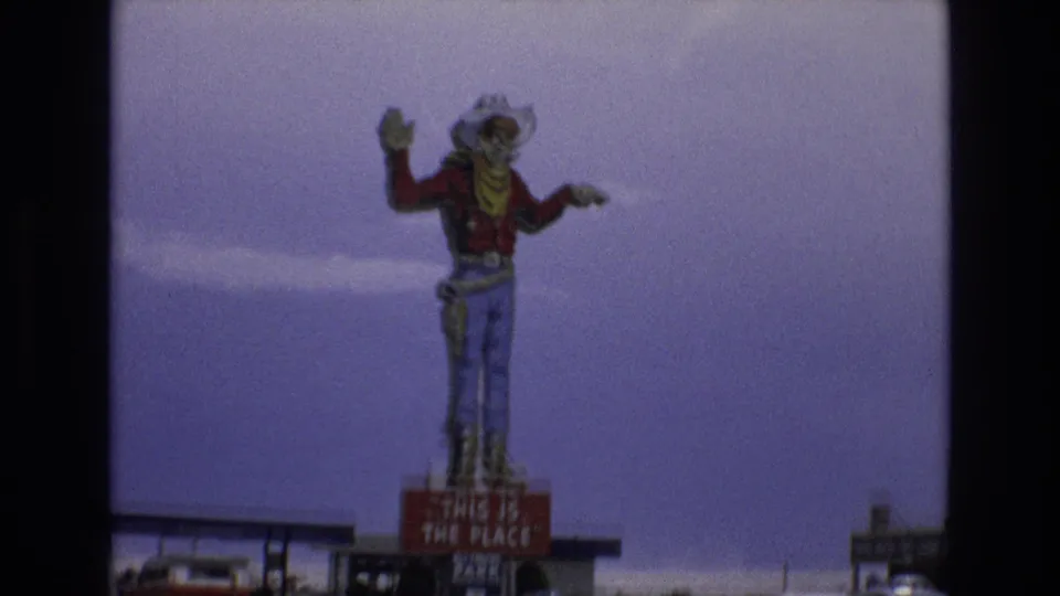 Closer 8mm frame of the Lake Tahoe roadside cowboy statue in a red shirt and jeans above the sign reading "THIS IS THE PLACE."