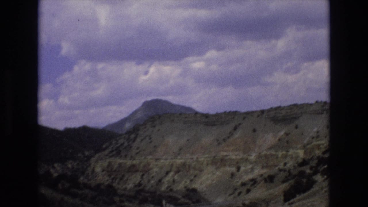 Paved road curving below layered hills with a distant peak and cloudy sky.
