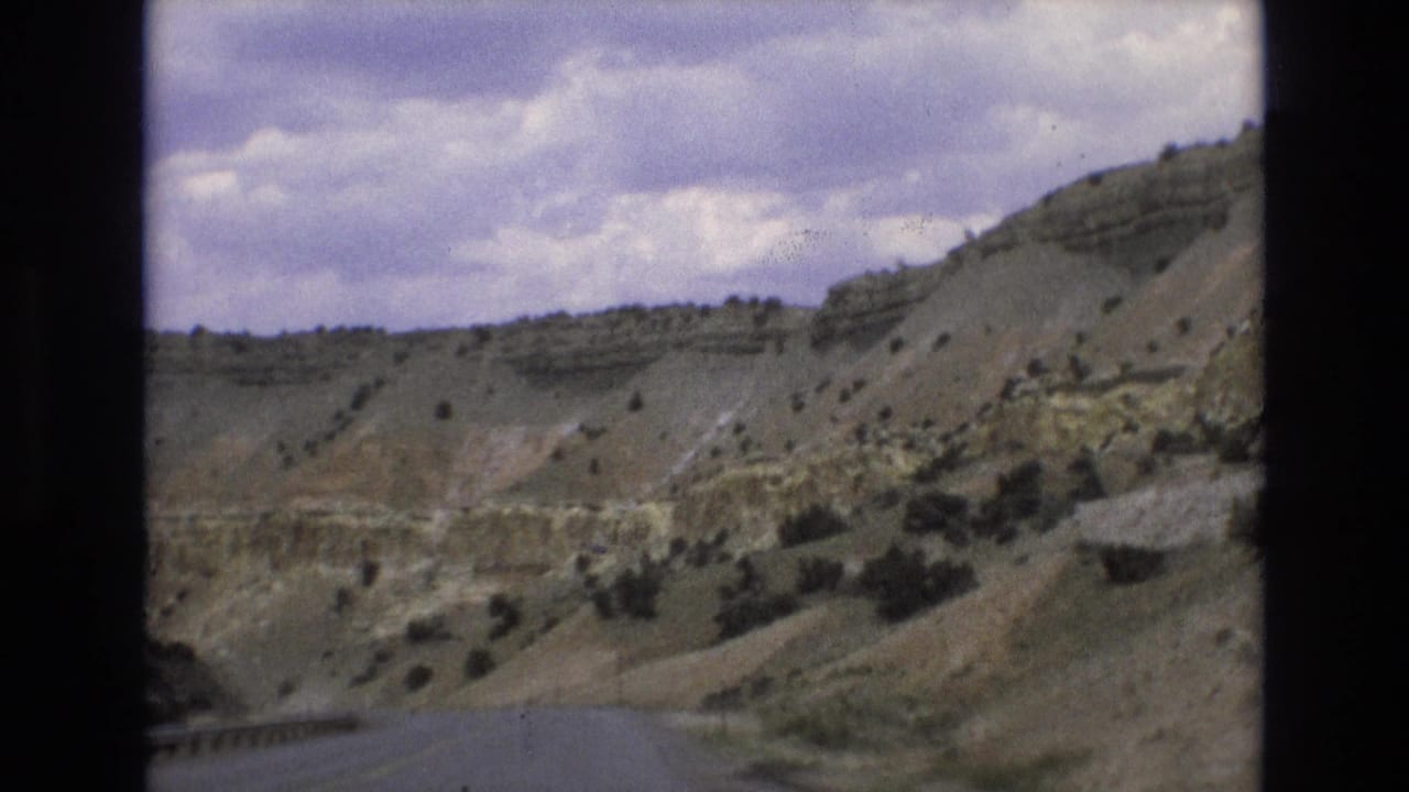 Empty paved road curving through dry hills under a cloudy sky.