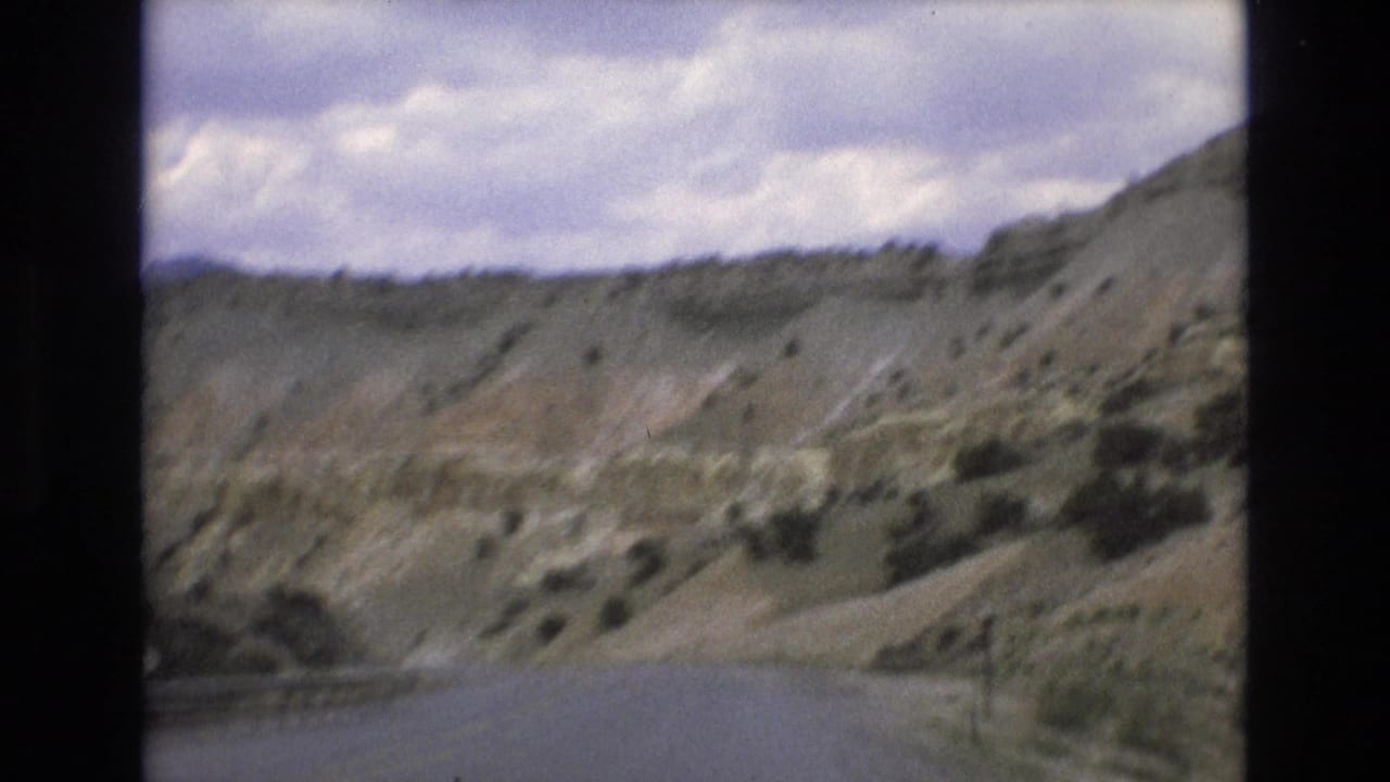 Curving road beside arid hills with scrub vegetation and clouds overhead.
