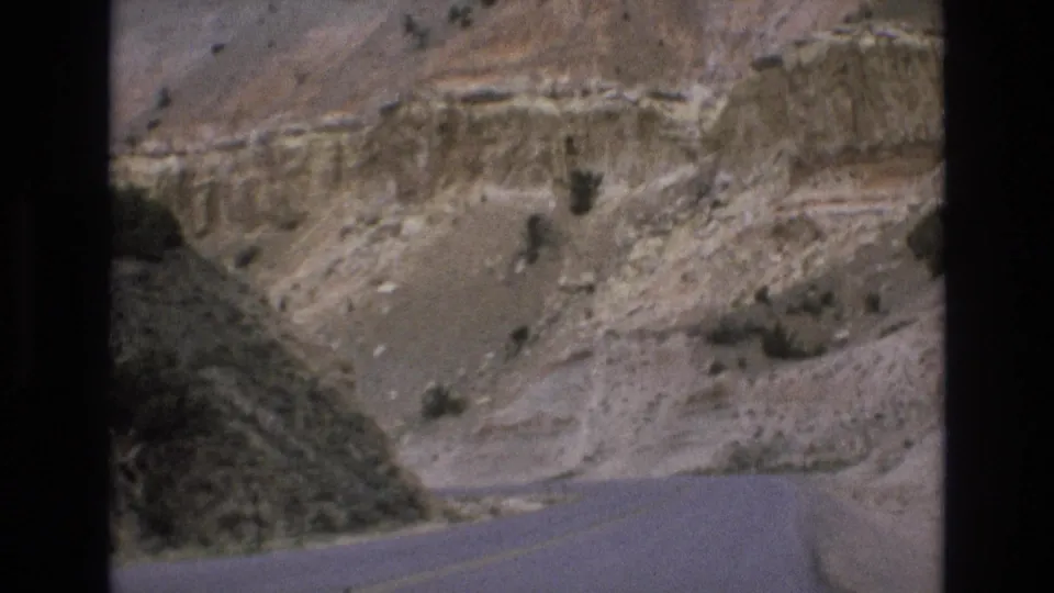 1973 Lake Tahoe, Nevada home-movie frame showing a paved road running beside exposed tan canyon slopes with scrub vegetation and soft 8mm motion blur.