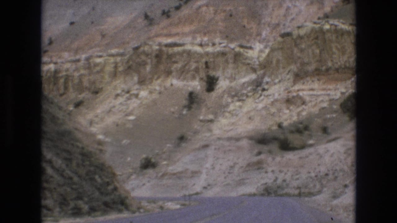1973 8mm home-movie frame from the Lake Tahoe, Nevada area showing a paved road bending through pale layered canyon terrain with scattered desert vegetation.