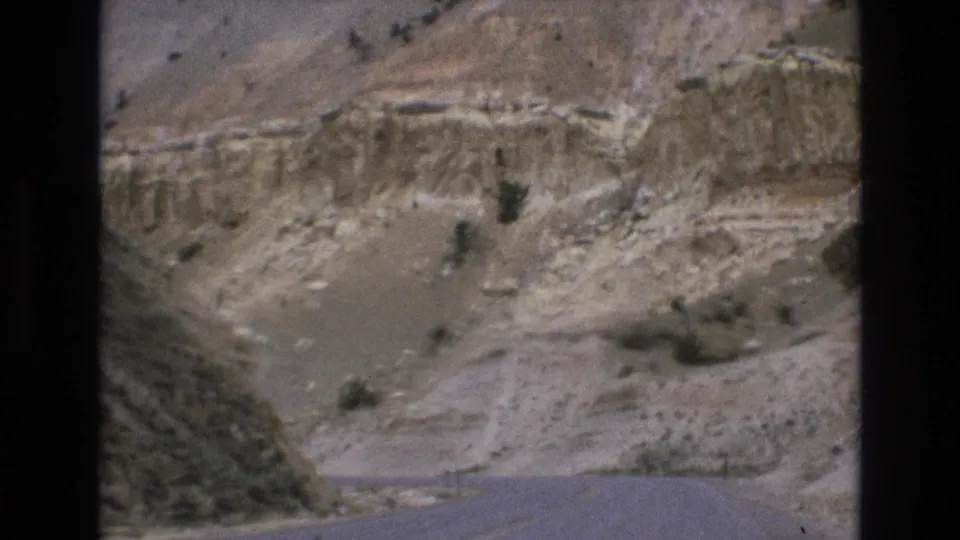 1973 8mm home-movie frame from the Lake Tahoe, Nevada area showing a paved road bending through pale layered canyon terrain with scattered desert vegetation.