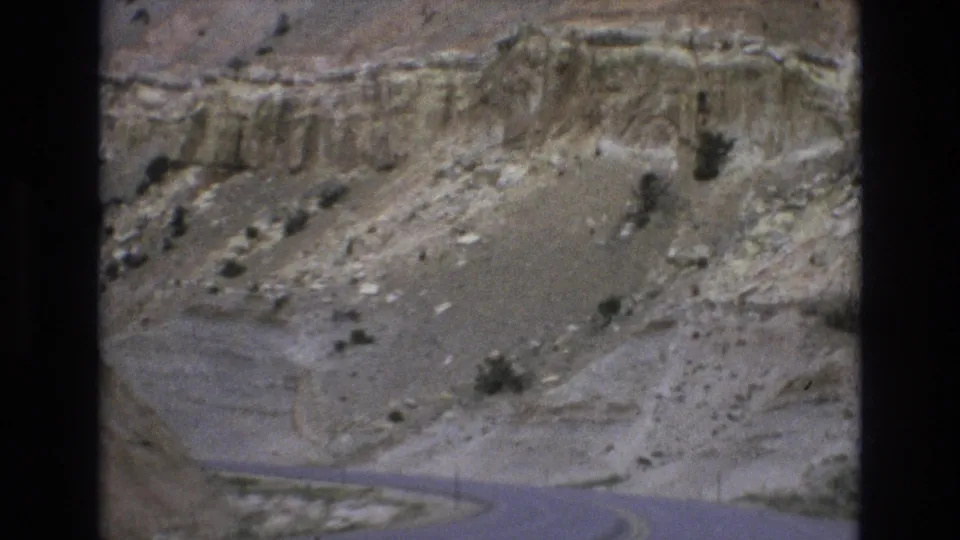 1973 Lake Tahoe, Nevada area road footage frame showing the canyon bottom, pale cliff bands, loose rock, and low brush from a moving home-movie viewpoint.
