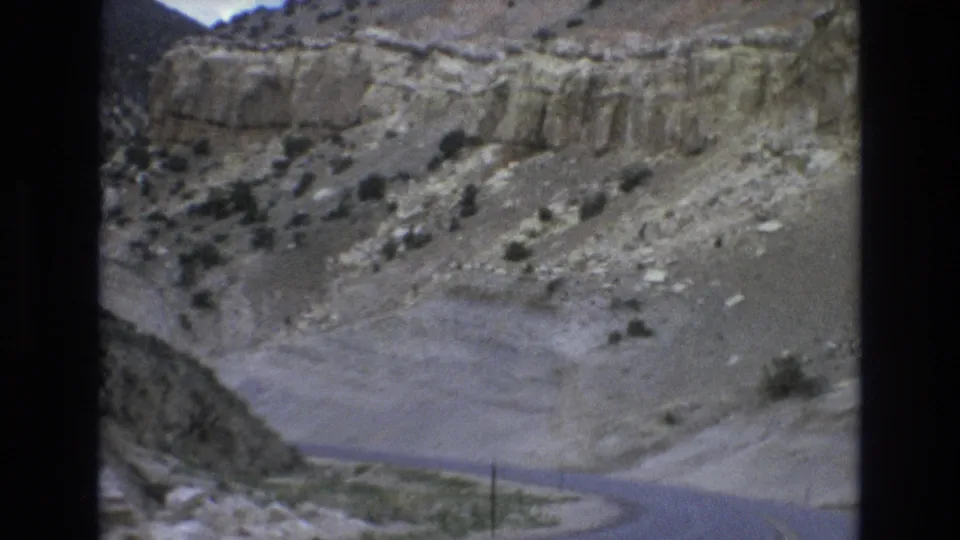 1973 8mm frame from the Lake Tahoe, Nevada area showing a road curving around rocky canyon slopes, sparse vegetation, and layered pale stone walls.