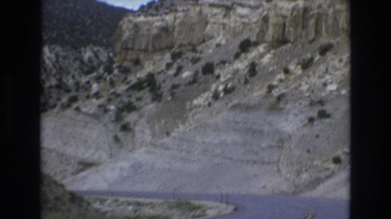 Mountain road curves between pale cliffs and sparse vegetation.