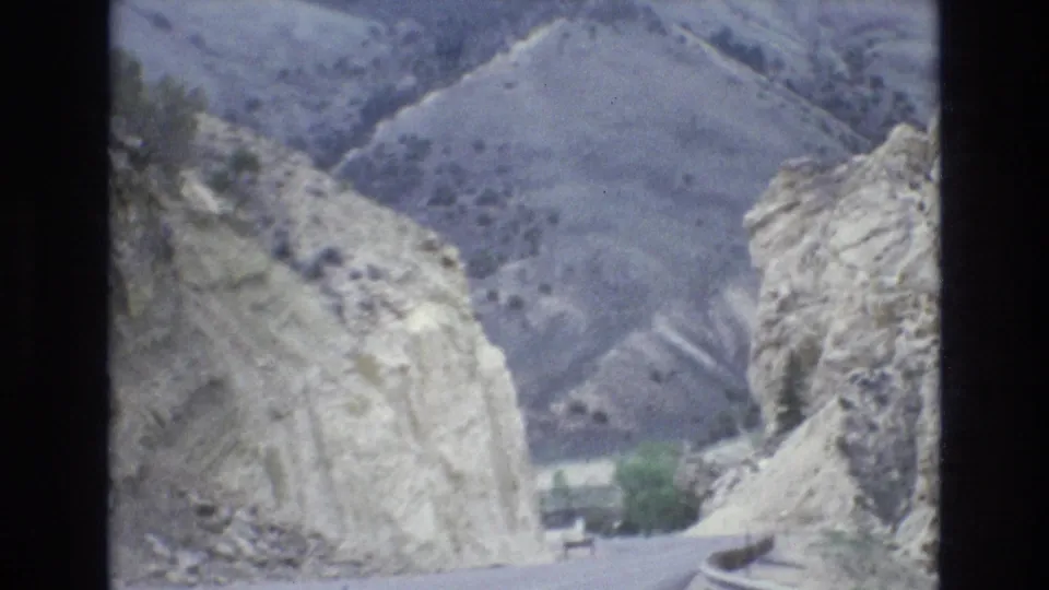 The road drops between pale canyon cuts toward sparse greenery in a 1973 8mm Lake Tahoe, Nevada travel view.
