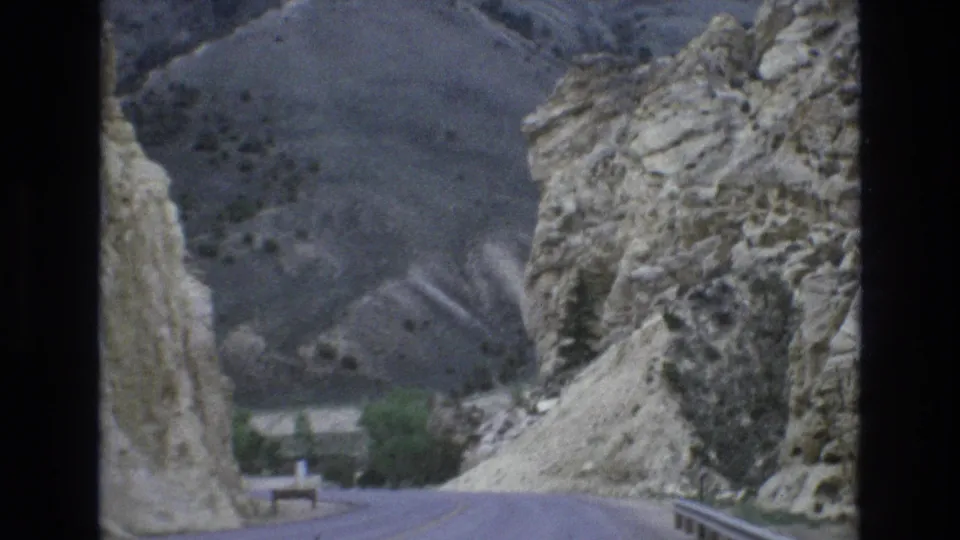 1973 Lake Tahoe, Nevada 8mm frame showing the roadway dropping through a rocky pass, with pale cliff faces and muted hills visible ahead.