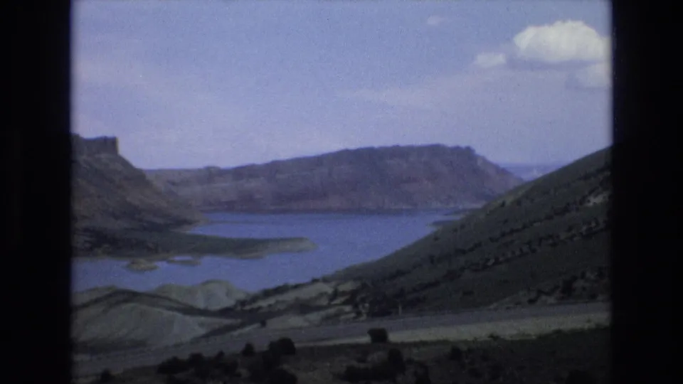 1973 8mm Lake Tahoe area overlook frame showing a broad blue lake below rugged ridgelines and dry foreground hills.