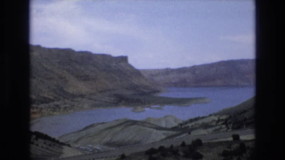1973 8mm Lake Tahoe area landscape frame with a lake basin, layered ridges, dry slopes, and sparse trees in the foreground.