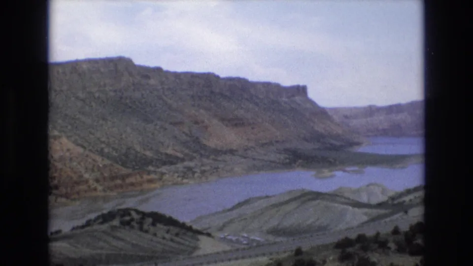 1973 8mm Lake Tahoe area scenic frame showing rugged mountain slopes above a blue lake, with sparse vegetation and muted home-movie color.