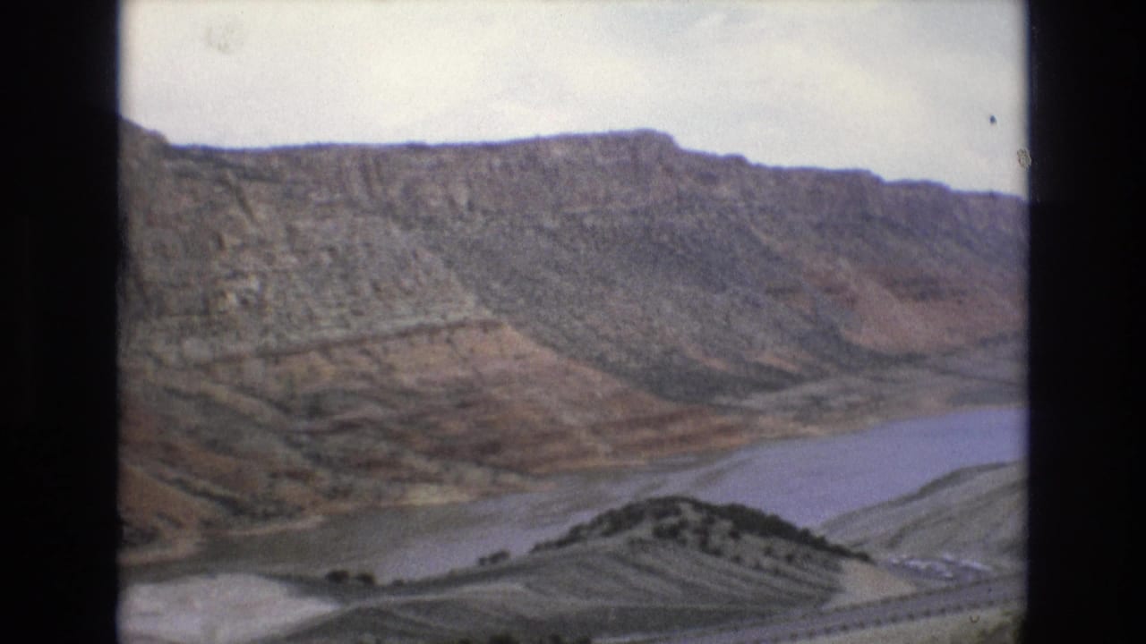 1973 8mm frame showing rugged Lake Tahoe, Nevada-area terrain with a broad water body curving below steep, layered hillsides.