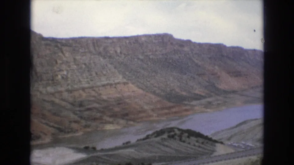 1973 8mm frame showing rugged Lake Tahoe, Nevada-area terrain with a broad water body curving below steep, layered hillsides.