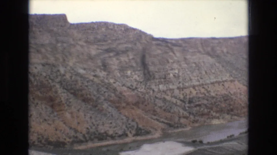 1973 8mm frame of rough Lake Tahoe, Nevada-area hillsides with visible erosion lines, scattered vegetation, and a narrow water surface along the lower frame.