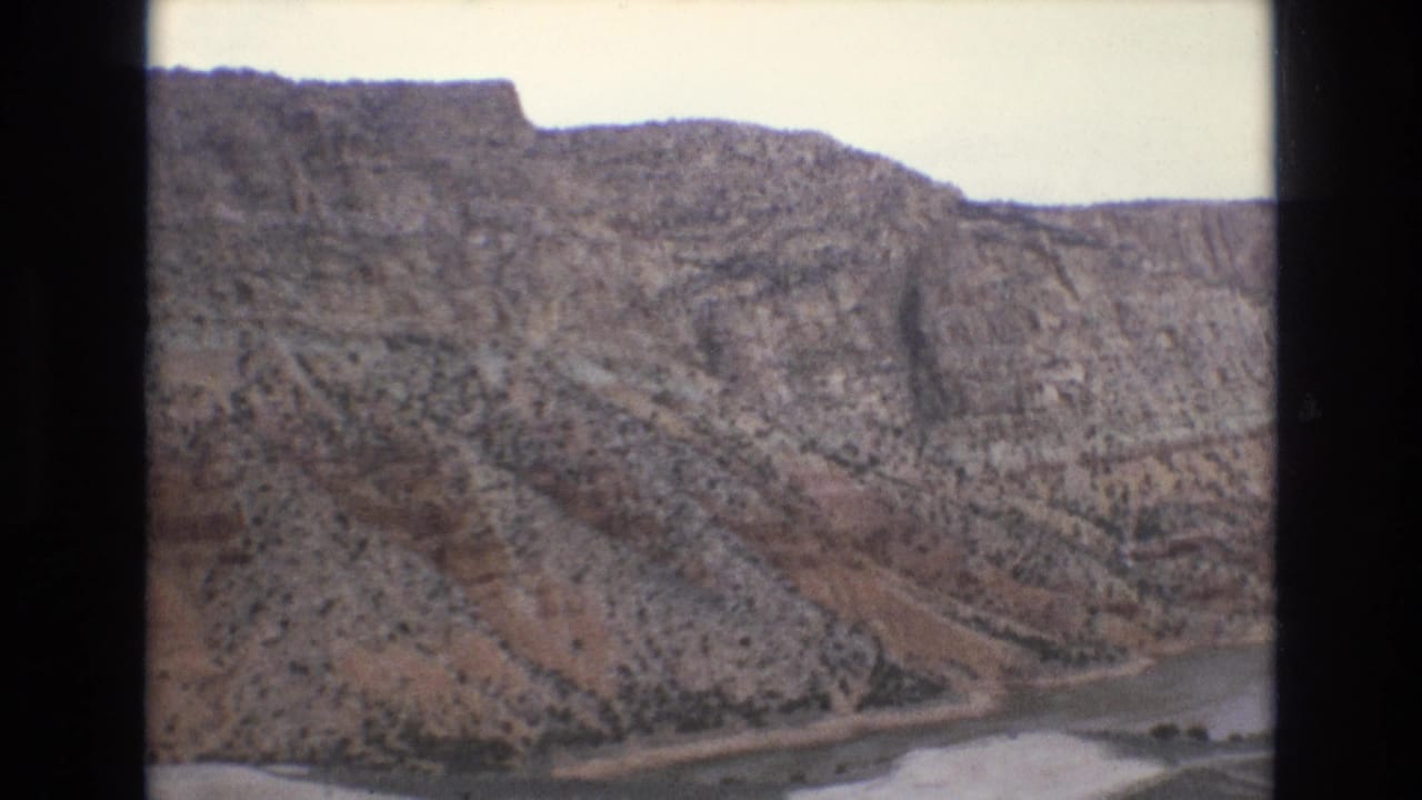 1973 Lake Tahoe-area 8mm frame showing a rocky mountain slope with sparse vegetation and a pale water edge below, bordered by dark film scan edges.