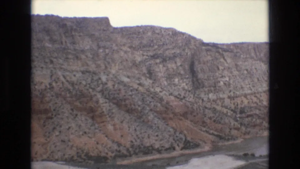1973 Lake Tahoe-area 8mm frame showing a rocky mountain slope with sparse vegetation and a pale water edge below, bordered by dark film scan edges.