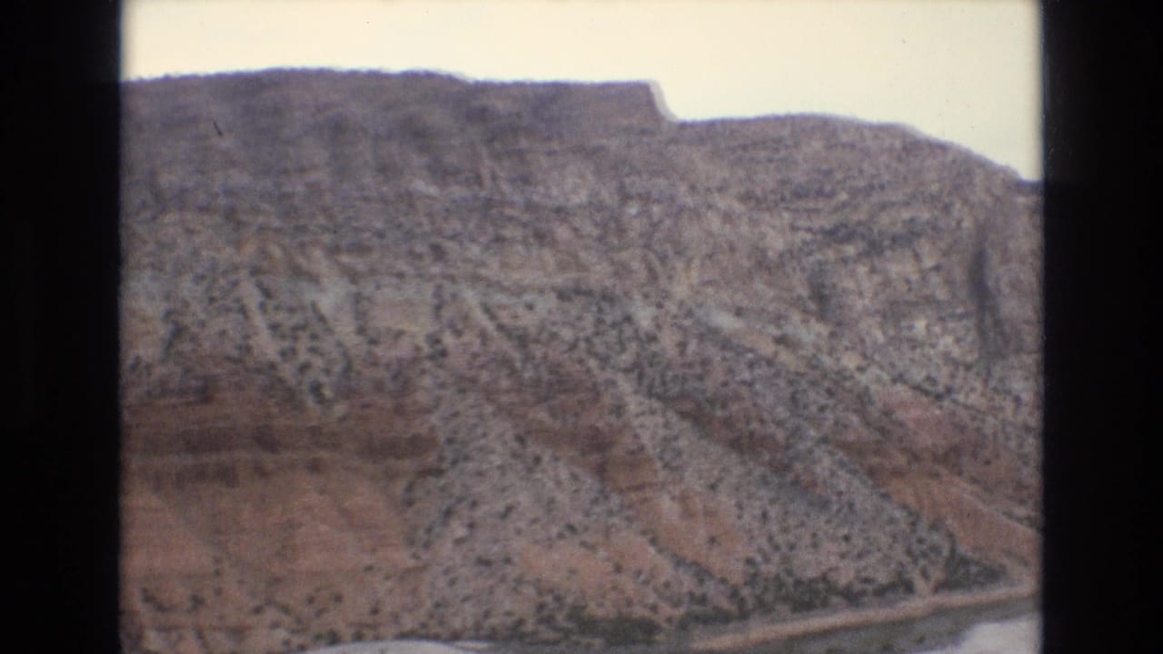 Rocky mountainside with sparse shrubs and a high ridge line.