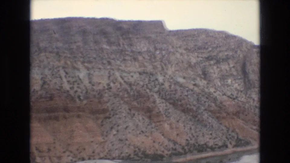 1973 Lake Tahoe-area 8mm frame showing a broad rocky mountainside with scattered shrubs and a flat-topped ridge under a pale sky.