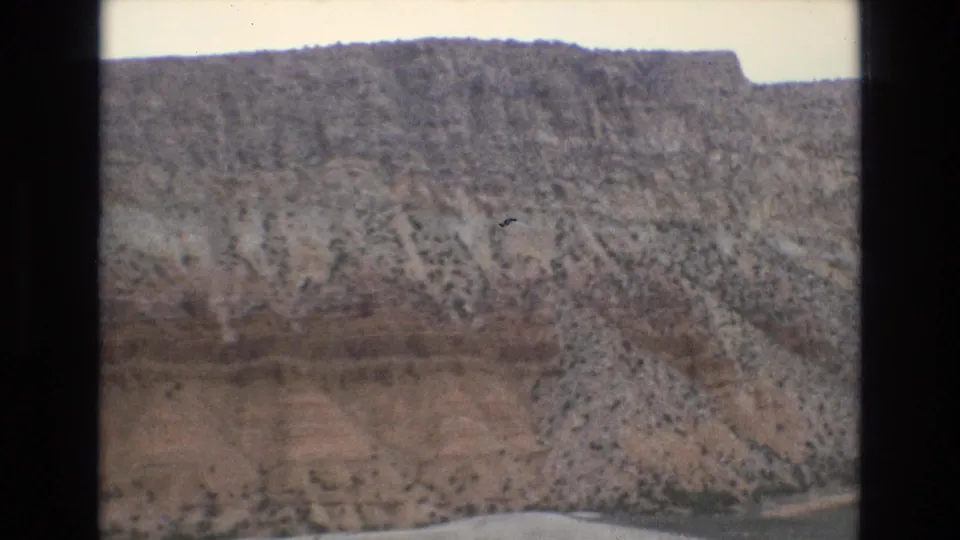 1973 Lake Tahoe-area 8mm frame showing a closer rocky slope with scrub vegetation and a narrow road or shoreline edge along the bottom of the frame.