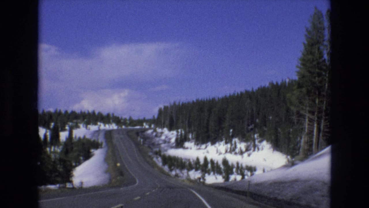 1973 8mm Lake Tahoe, Nevada car-perspective view of a two-lane mountain road curving through snow-covered evergreen terrain.