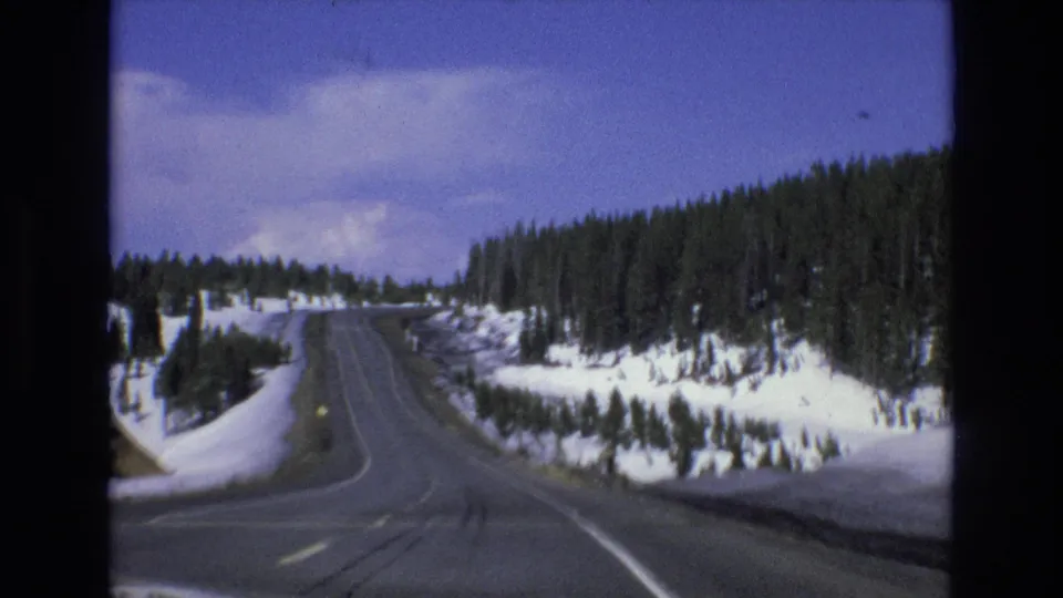 Car-view 8mm frame of a winter road climbing through pine-covered slopes near Lake Tahoe, Nevada, with snow lining the shoulders.