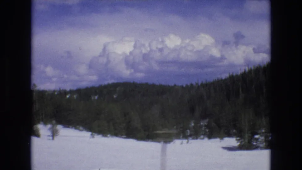 1973 Lake Tahoe, Nevada home-movie frame looking across snow, evergreen forest, and low hills under a large cloud bank.