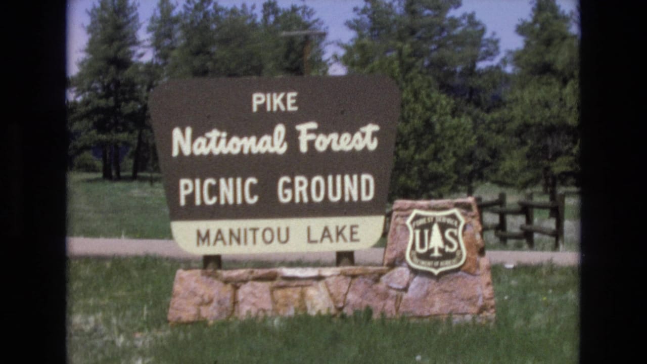 Manitou Lake picnic-ground sign with U.S. Forest Service shield in a grassy forest setting.